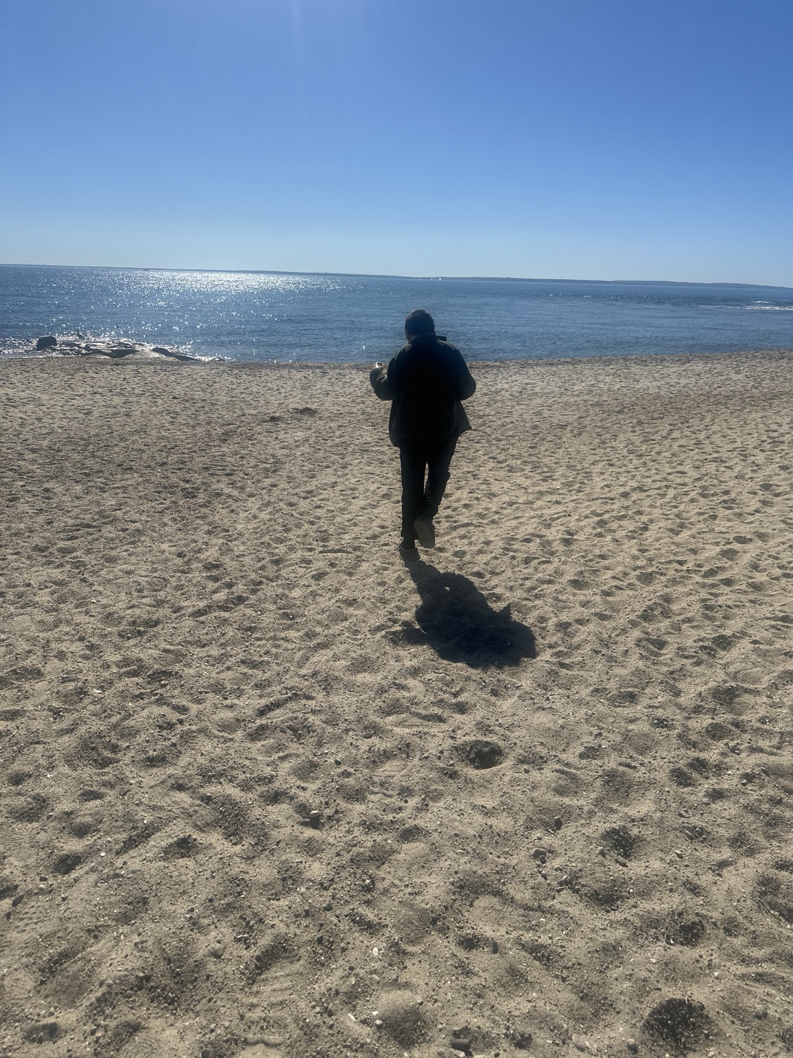 James walking across the sand toward the shoreline, photographed from behind with open space around him.