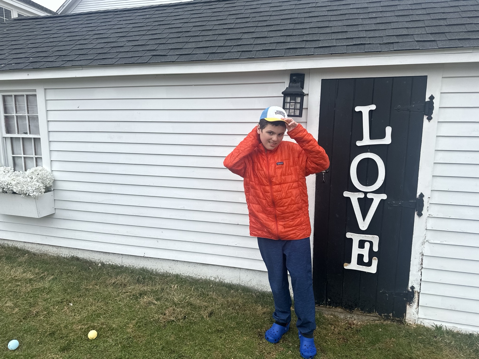 A teenager touches the brim of a cap beside a black farm door with large white letters spelling LOVE.