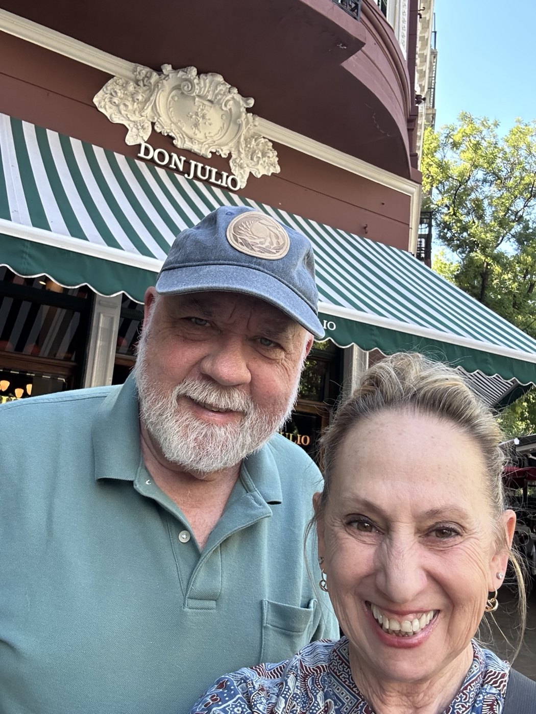 Mom-Mom and Grandpa Steve smiling together in front of Don Julio's green-and-white striped awning in Buenos Aires.
