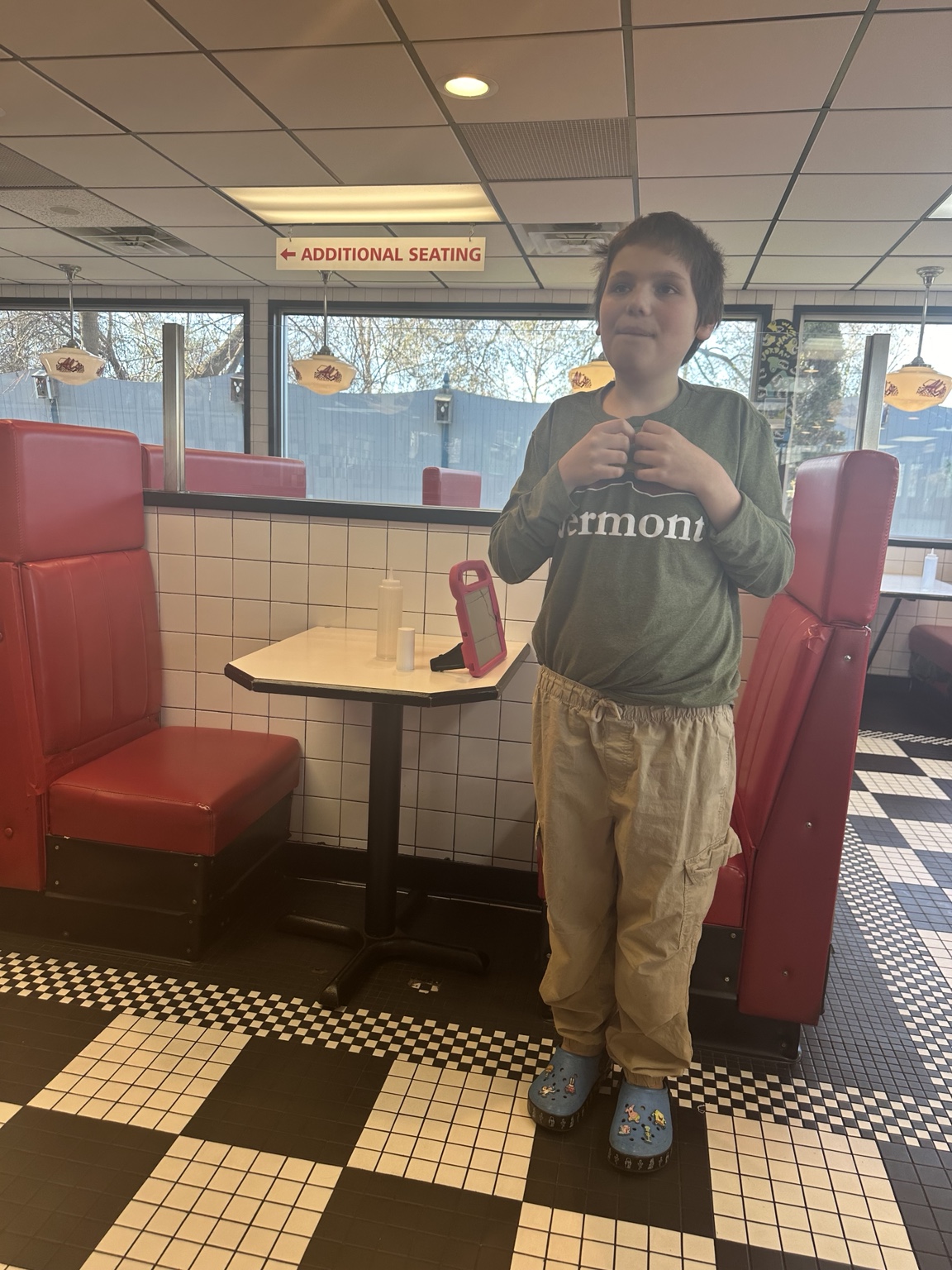 James in a green Vermont shirt beside a red booth at Al’s French Frys; his pink-cased device is on the table.