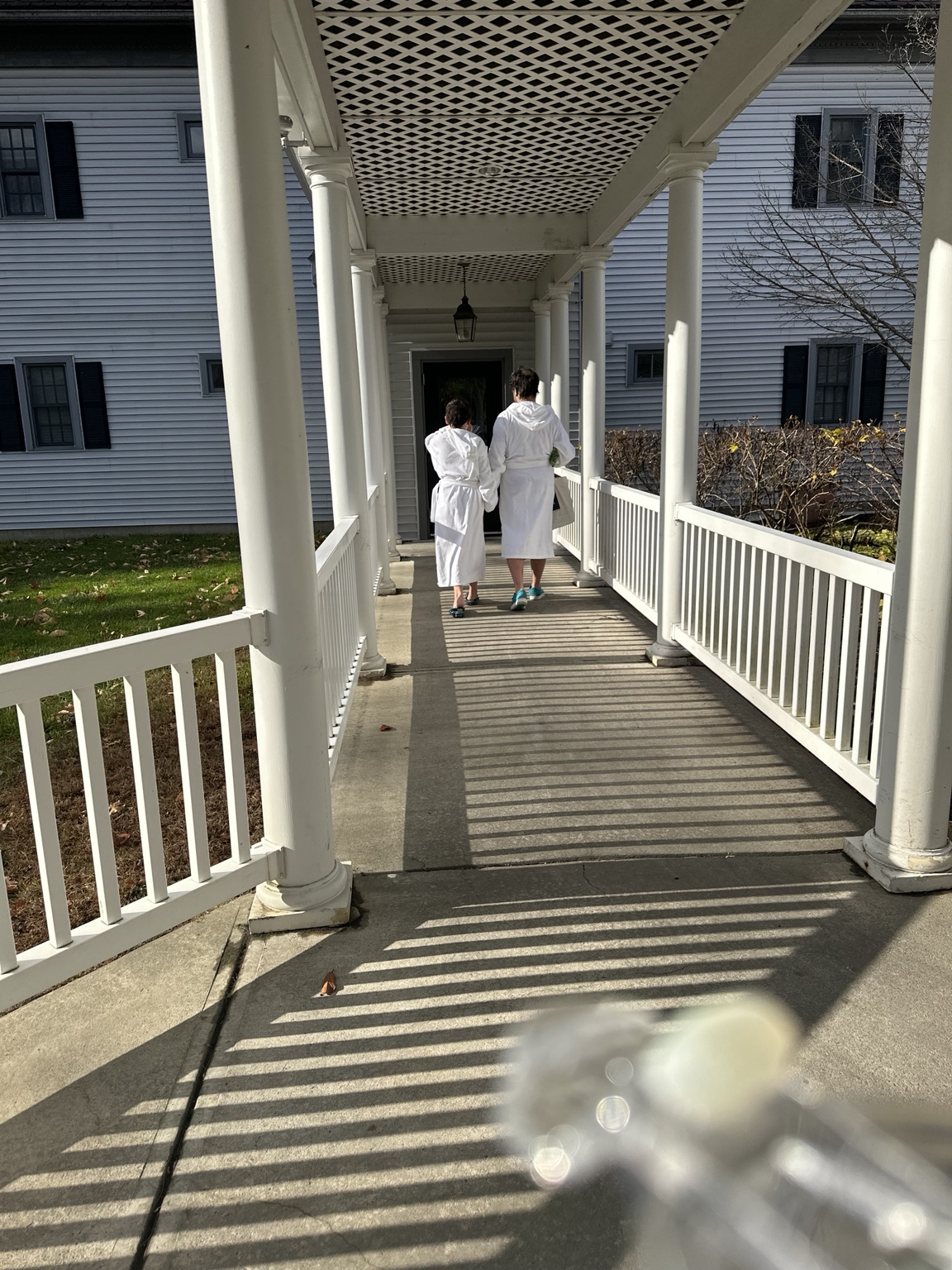 Two family members in white bathrobes walking beneath a covered walkway with white columns.