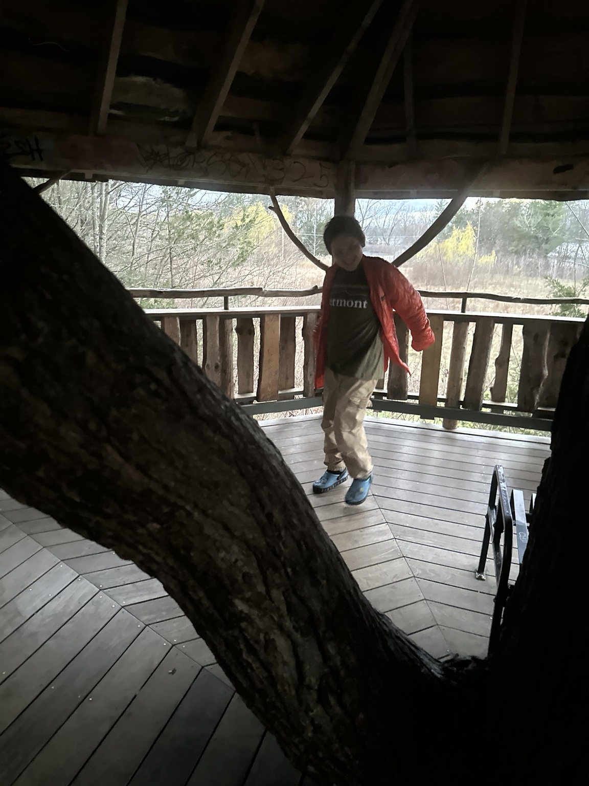 James in an orange jacket inside the Oakledge Park treehouse, with a large tree trunk in the foreground.