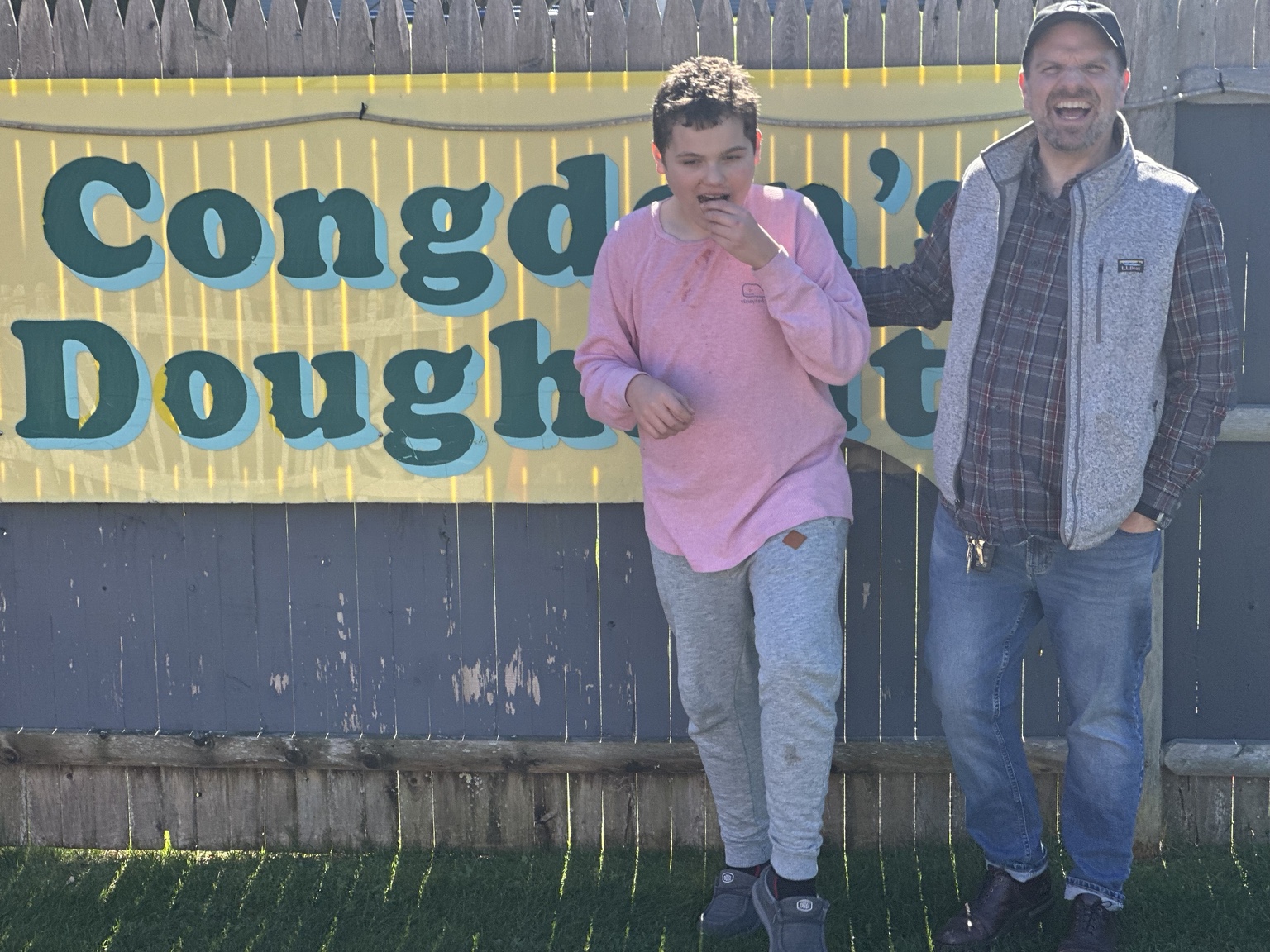 James enjoying a doughnut beside his dad in front of the yellow Congdon’s Doughnuts sign in Wells.
