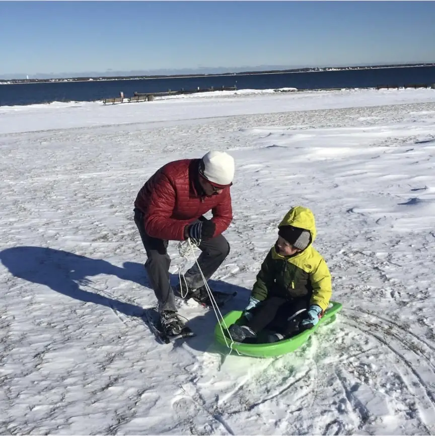 A family winter outing at Fort Taber in New Bedford, with snowshoes and a bright green sled beside the ocean.