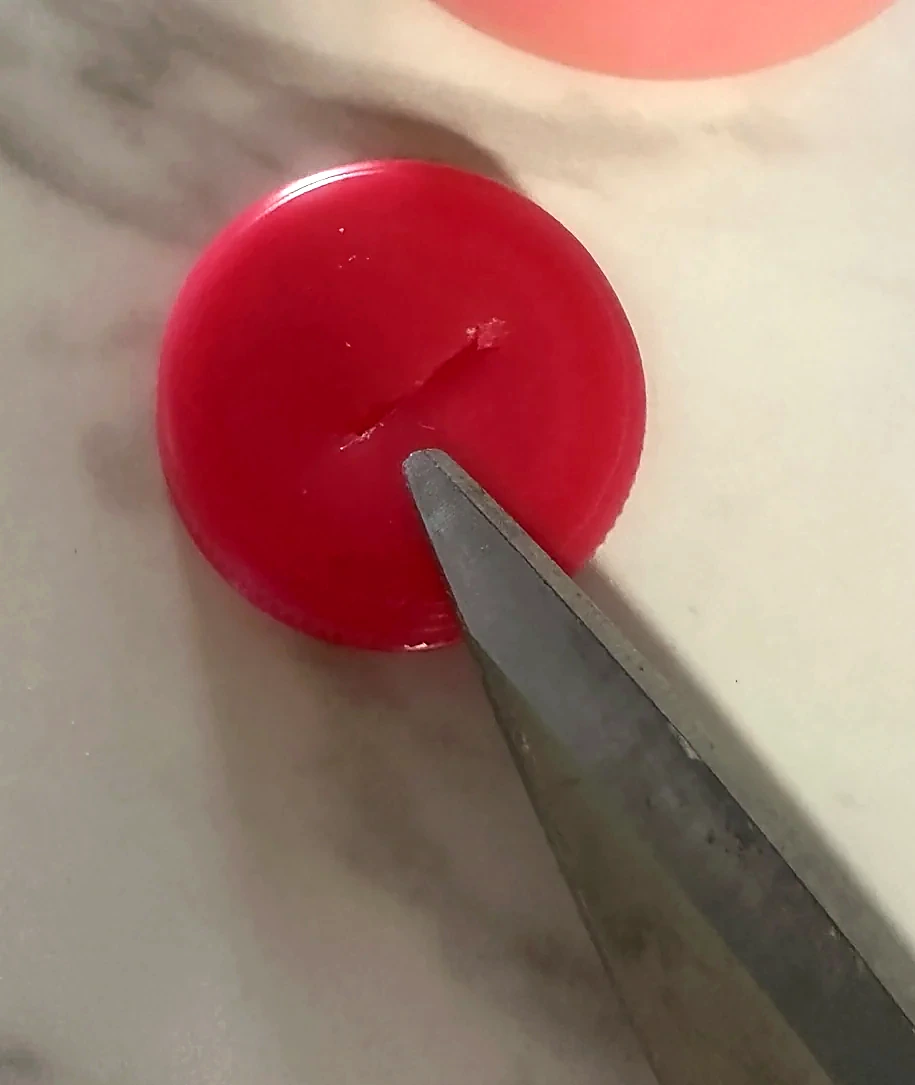 Original close-up photograph of the small slit in the red cap beside a pair of scissors.