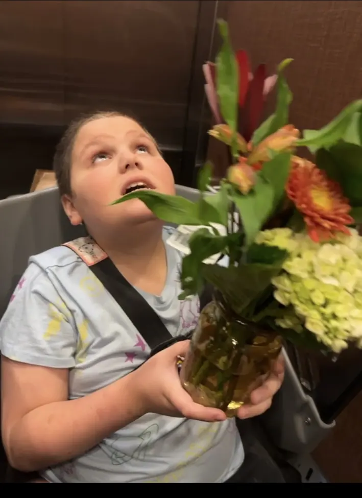 A family member seated in Caroline’s Cart at Wegmans, holding a bouquet of flowers.