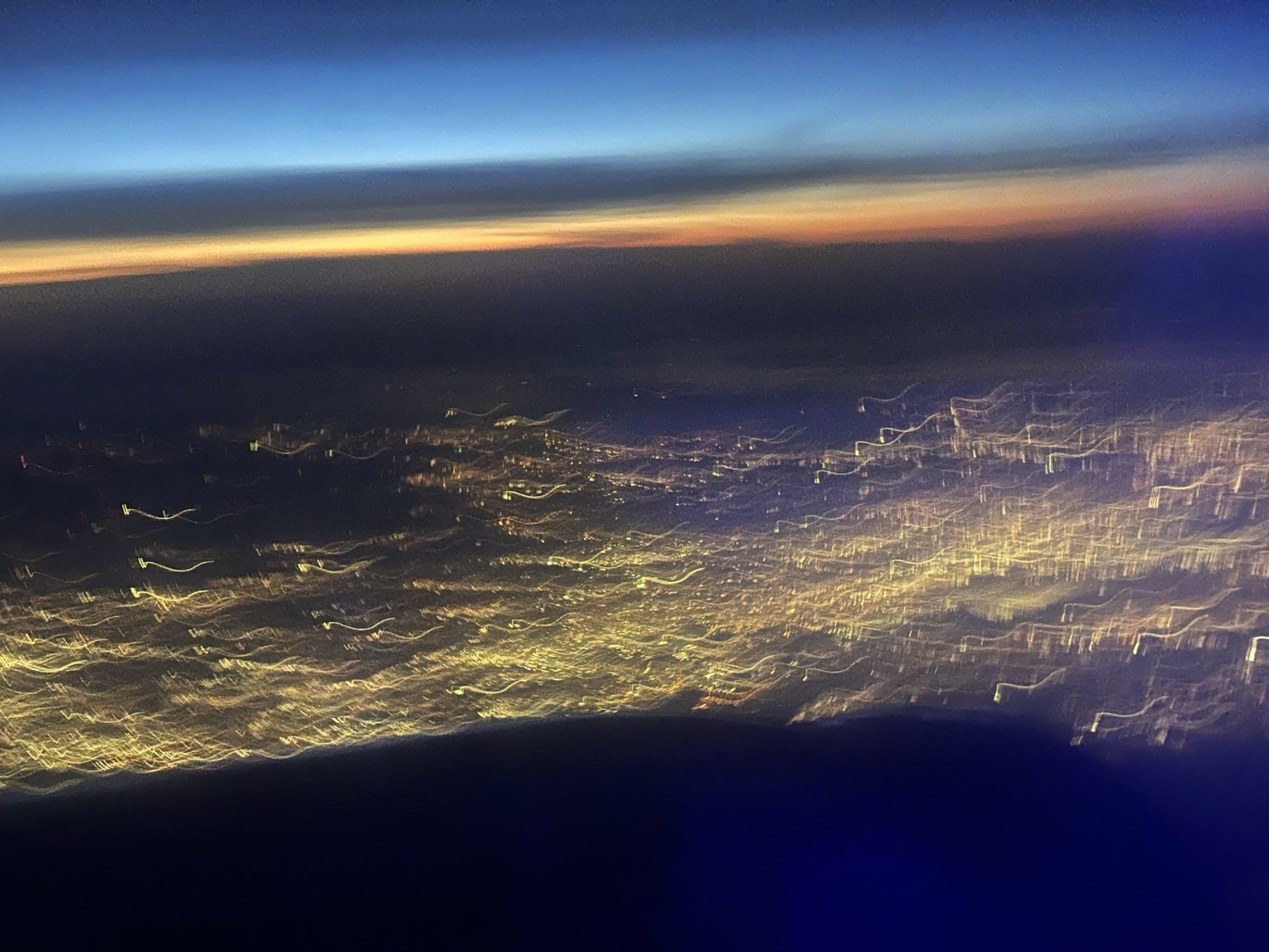 City lights below a sunset, photographed from an airplane.