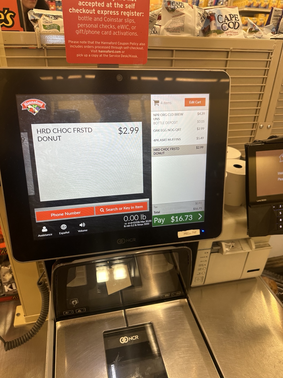 Hannaford self-checkout listing cold brew at $4.29, a five-cent bottle deposit, Oakhurst eggnog at $2.99, assorted muffins at $5.49 and chocolate-frosted donuts at $2.99. Tax is $0.92 and the displayed total is $16.73.