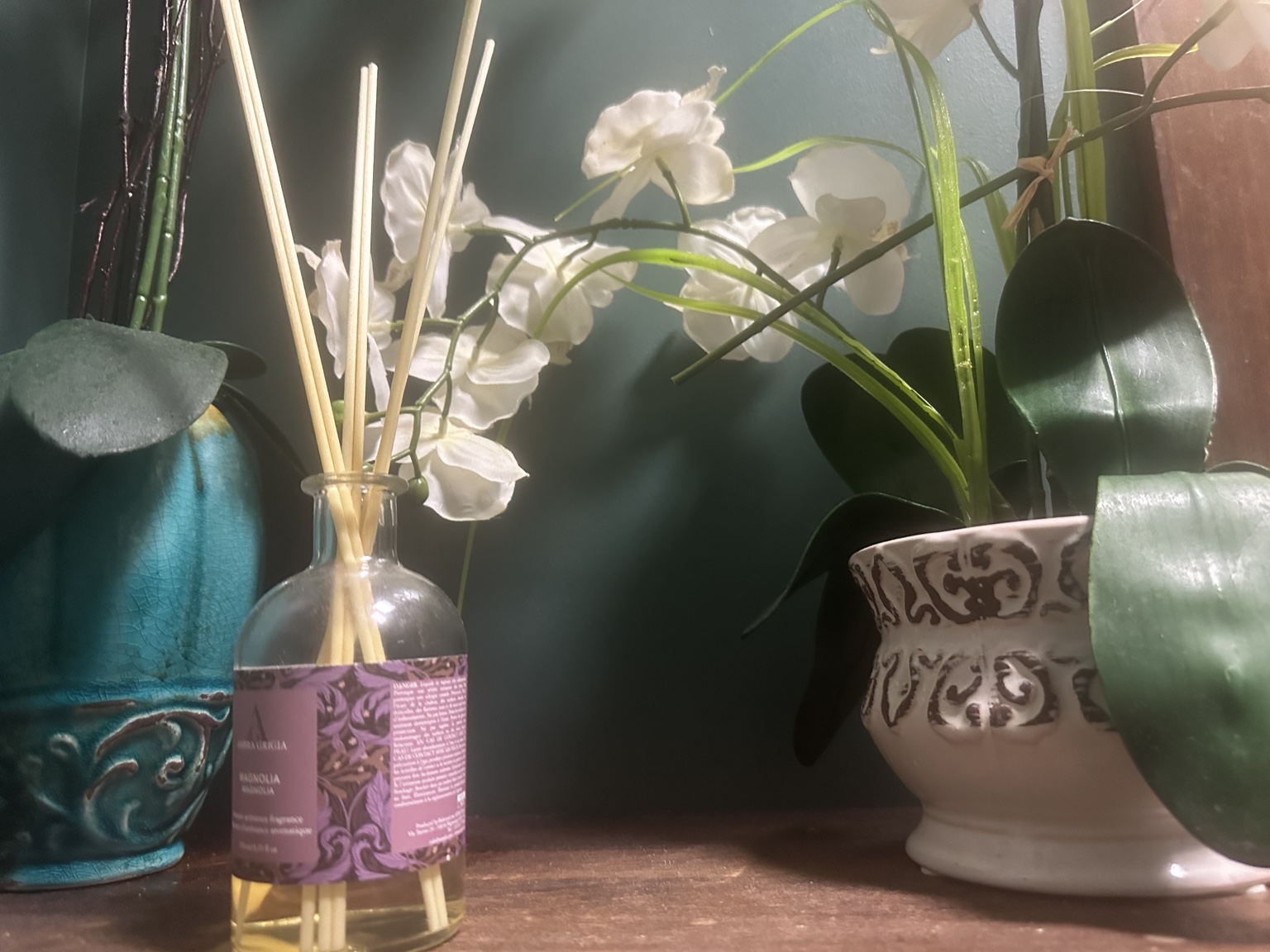 White orchid blooms, patterned ceramic pots, and a reed diffuser against the restaurant’s green wall.