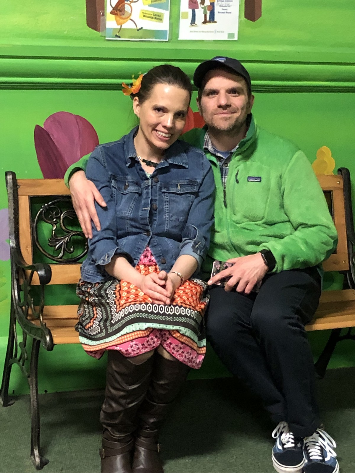 Two adults smiling together on a bench in a brightly colored museum exhibit.