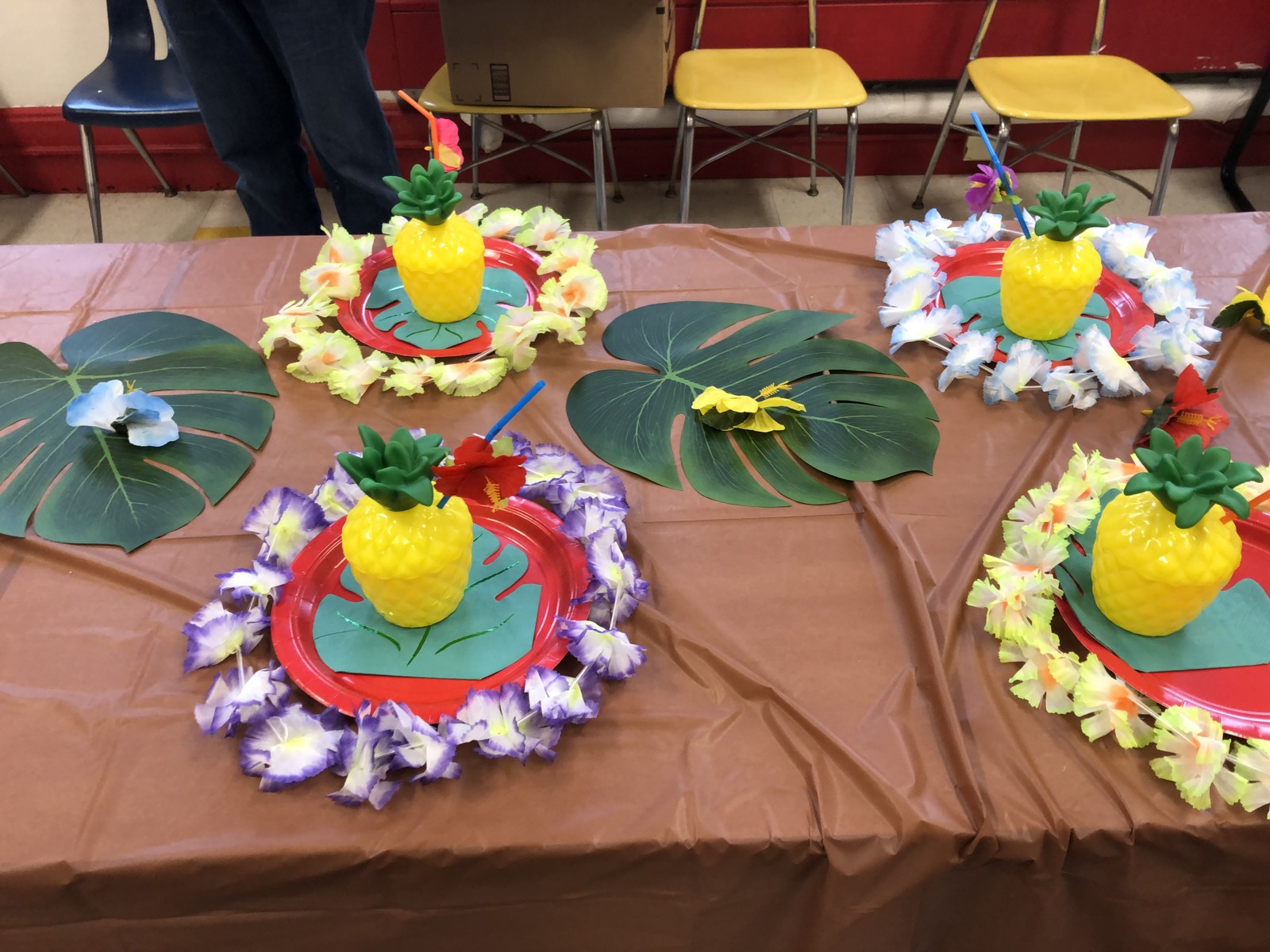 Yellow pineapple cups, colorful flower leis and red plates arranged on the birthday table.