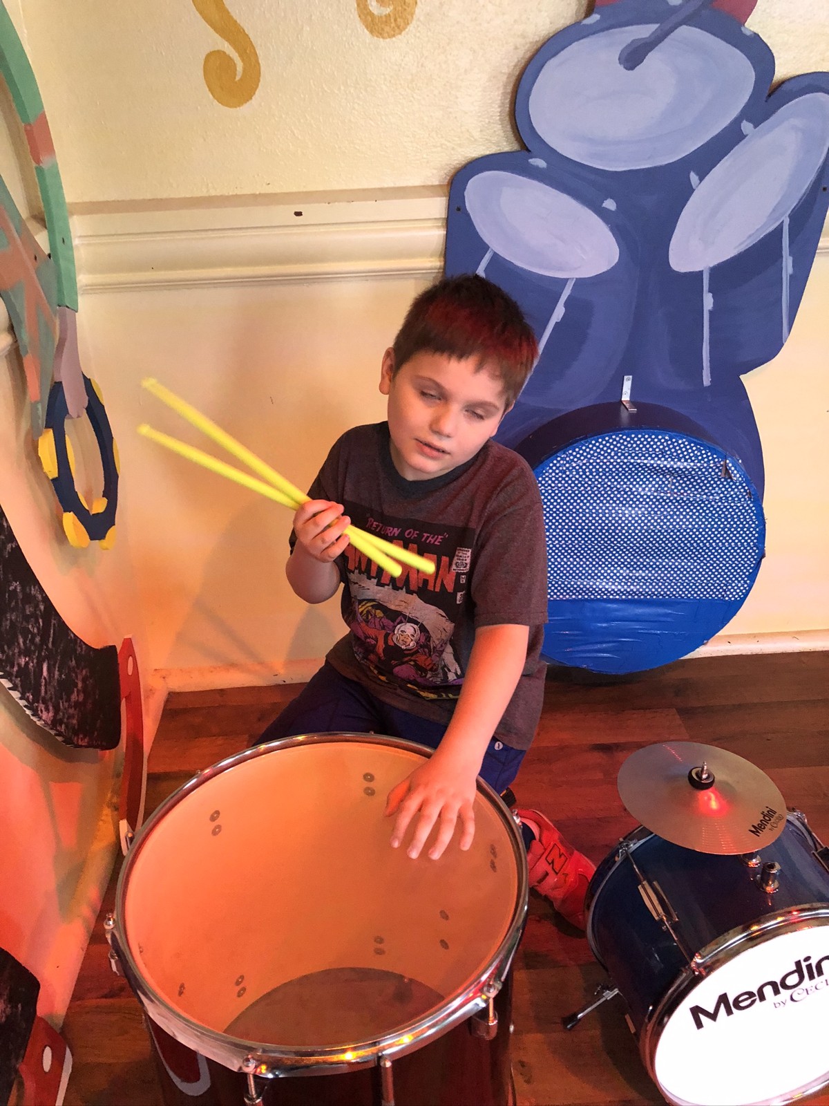James exploring a drum kit in front of a colorful music mural at the museum.