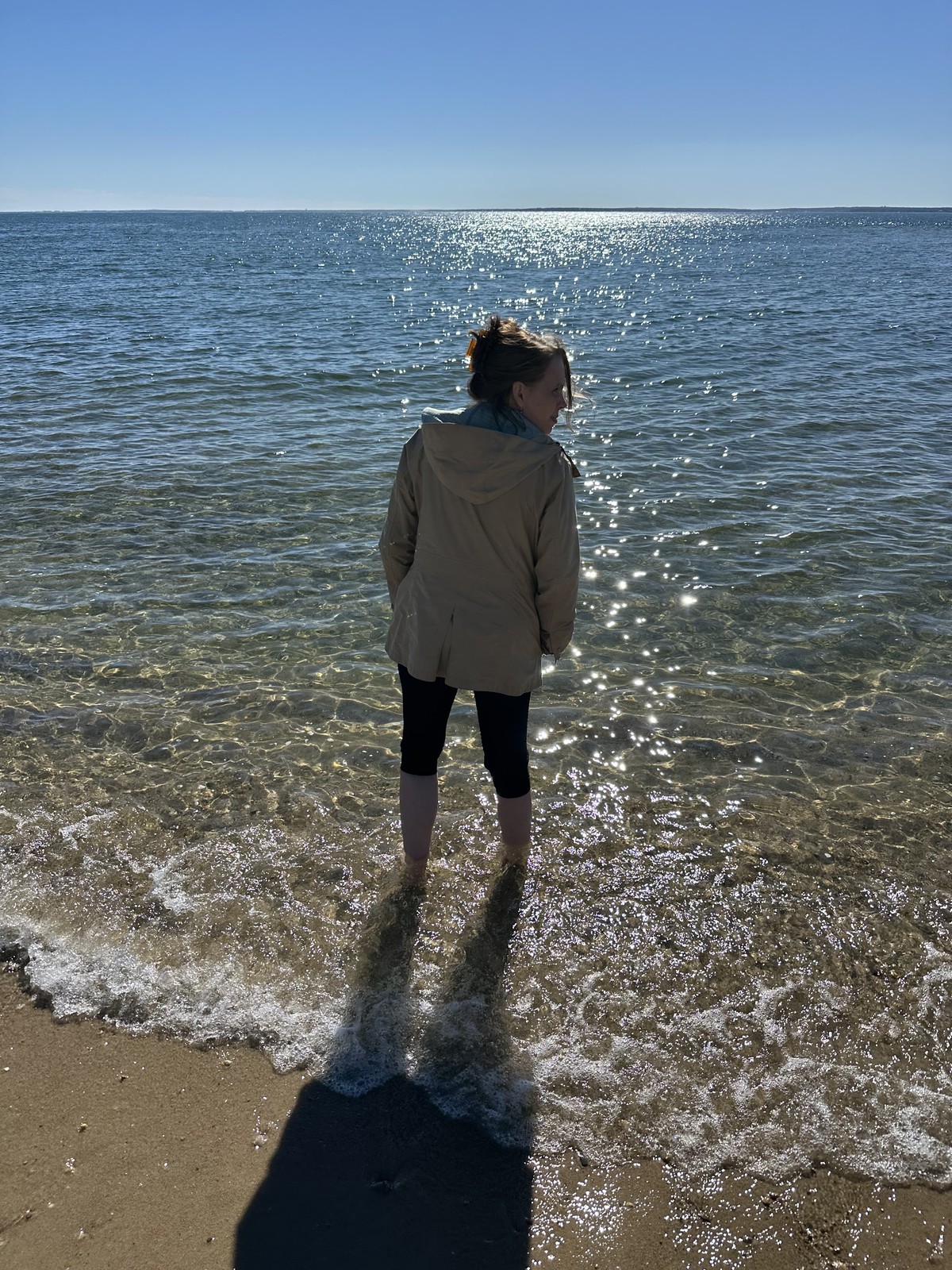 James’s mother stands in clear ankle-deep water as a small wave reaches the sand.