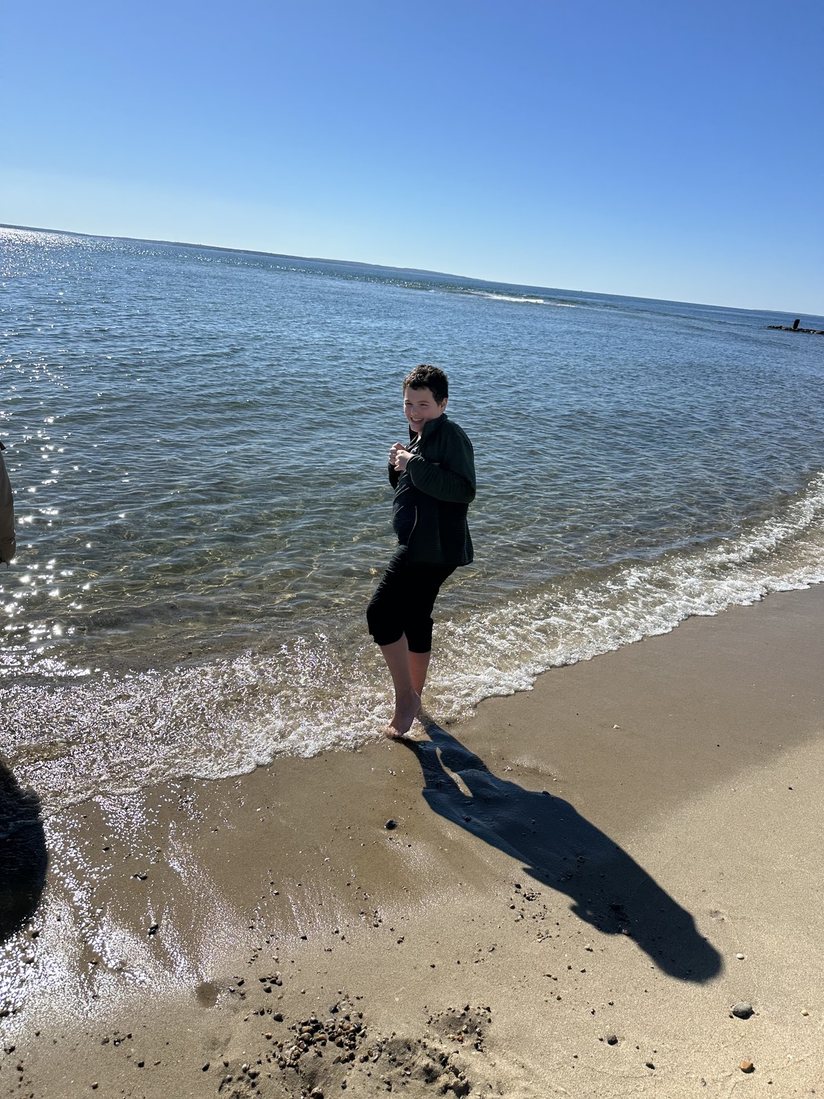 James turns toward the camera while standing barefoot at the edge of a small wave.