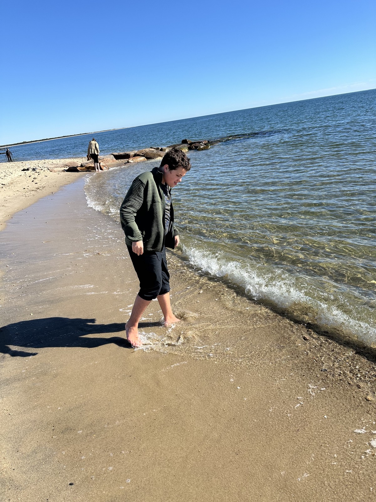 James watches a wave wash around his feet beside the stone jetty.