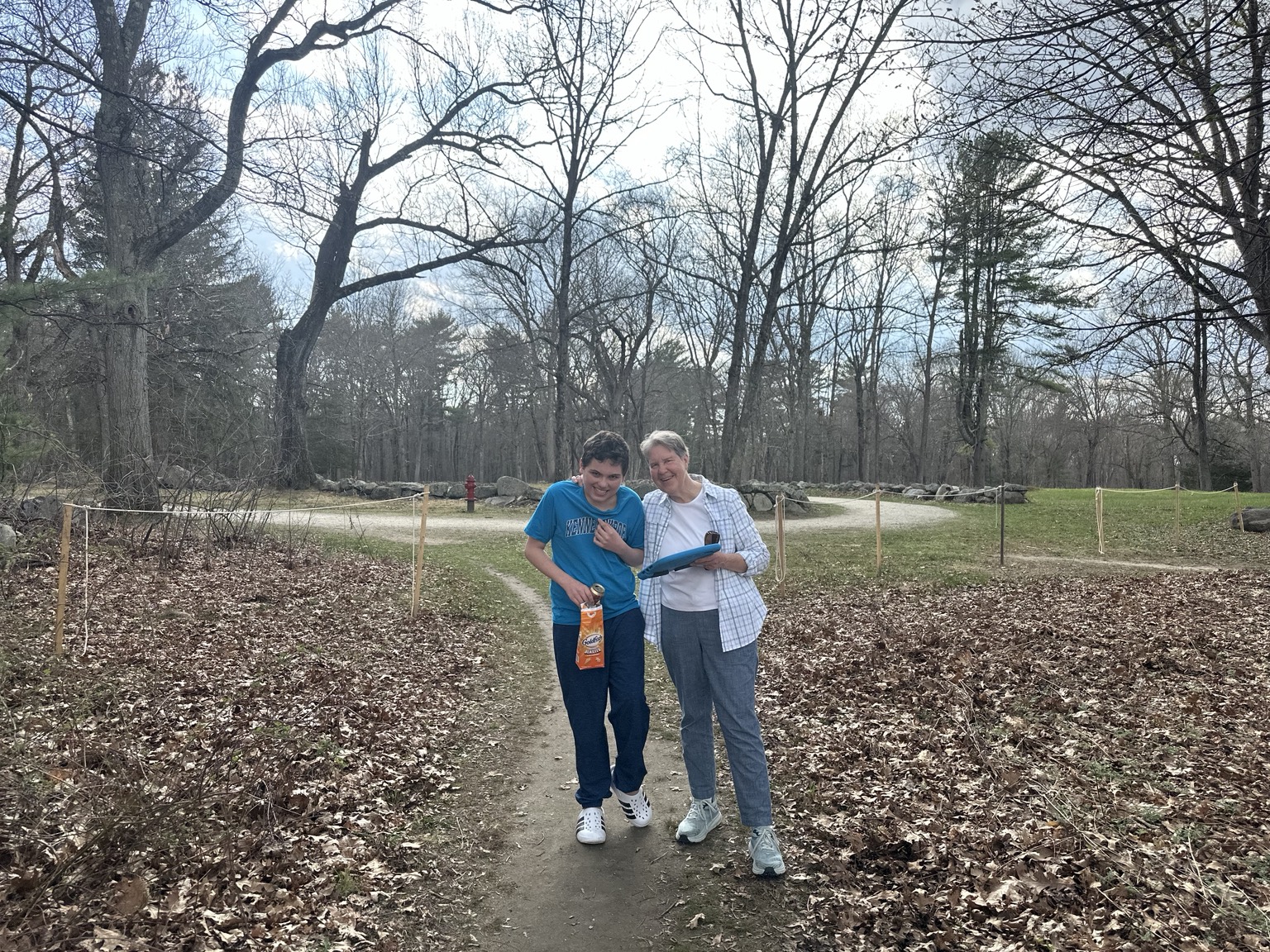 James and his great-aunt Susan smiling together on a woodland path bordered by leaves and stone walls.