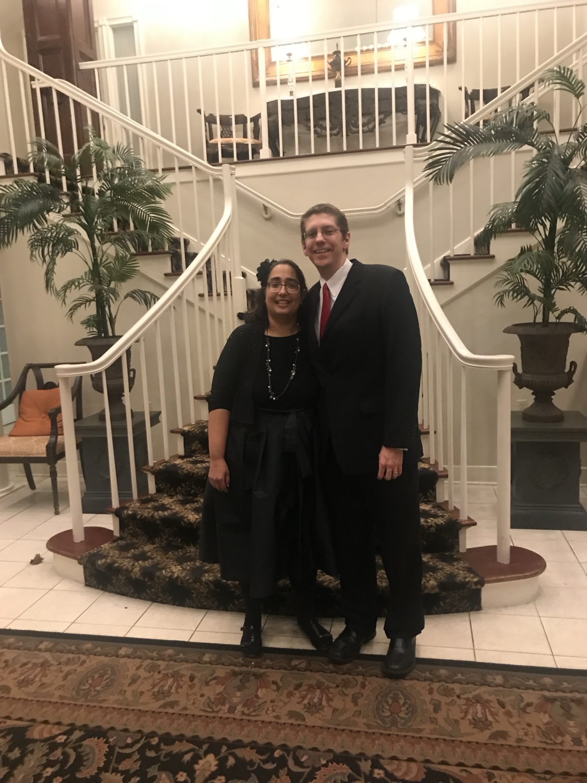 Two wedding guests smiling beneath a wide split staircase in the lobby.