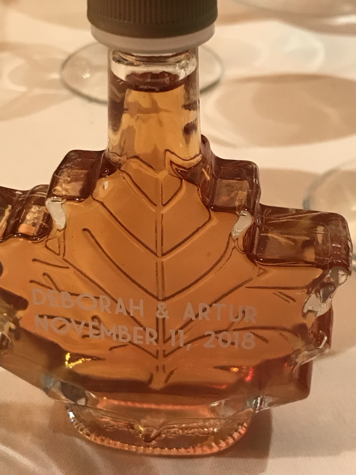 A maple-leaf-shaped amber wedding favor bottle engraved with Deborah and Artur's names and the date November 11, 2018.