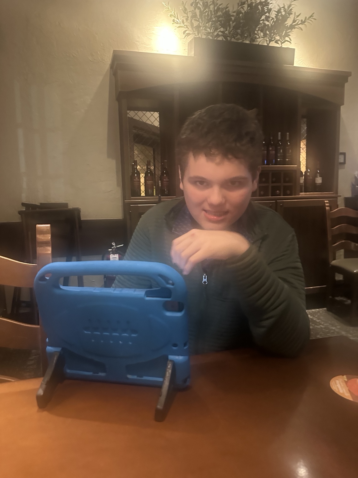 James looks toward the camera at Olive Garden, with his blue AAC communication device in front of him.