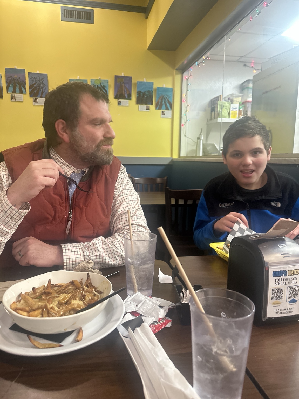James and an adult family member seated together at Omar’s Bistro, with food and drinks on the table.