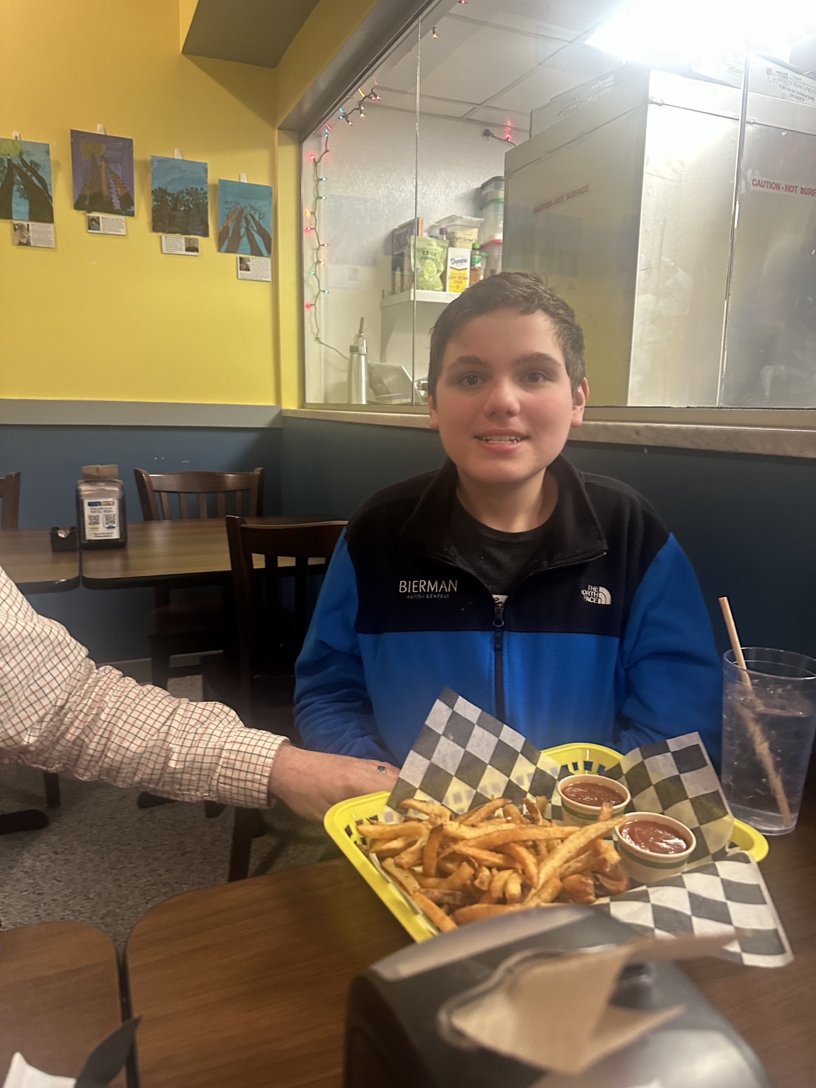 James seated in front of his fries at Omar’s Bistro, with yellow walls and an open kitchen behind him.