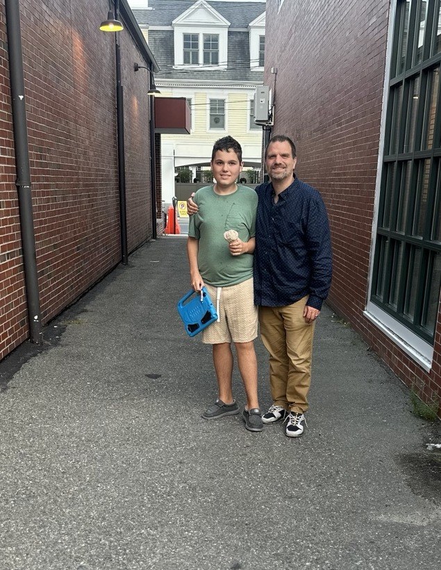 Two family members standing in a brick-lined passage, one holding an ice cream cone and a blue tablet case