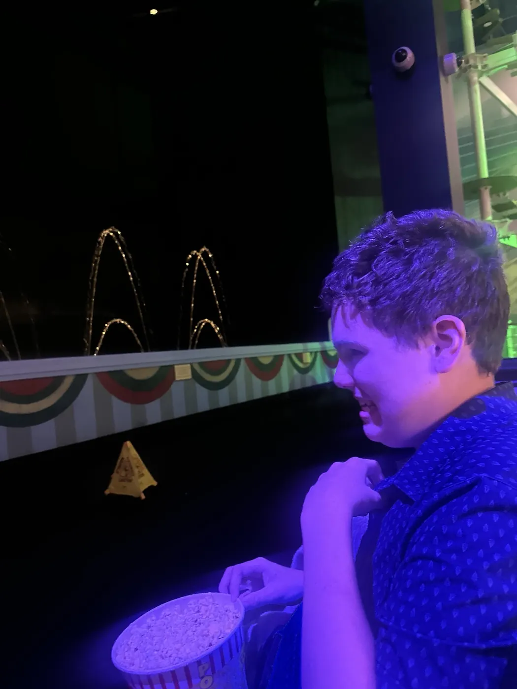 James sits beside the fountain show with a striped tub of popcorn as purple light illuminates the scene.