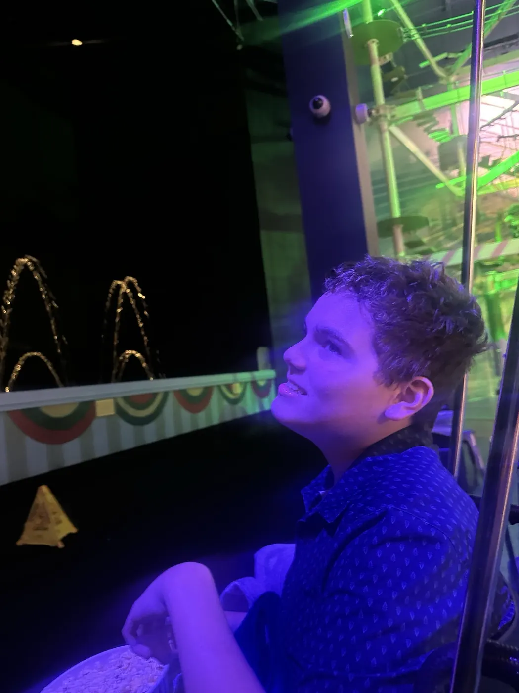 James looks toward illuminated arches of water at Jordan’s Furniture’s indoor fountain display, under purple and green lights.