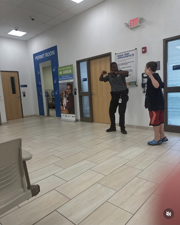 James and a security guard dance with their arms raised beside the doors in an RMV waiting room.