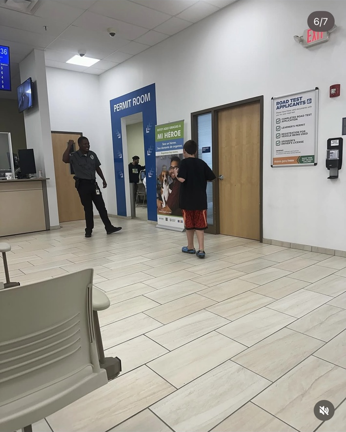 The guard smiles and raises one hand while James faces him across the waiting-room floor.