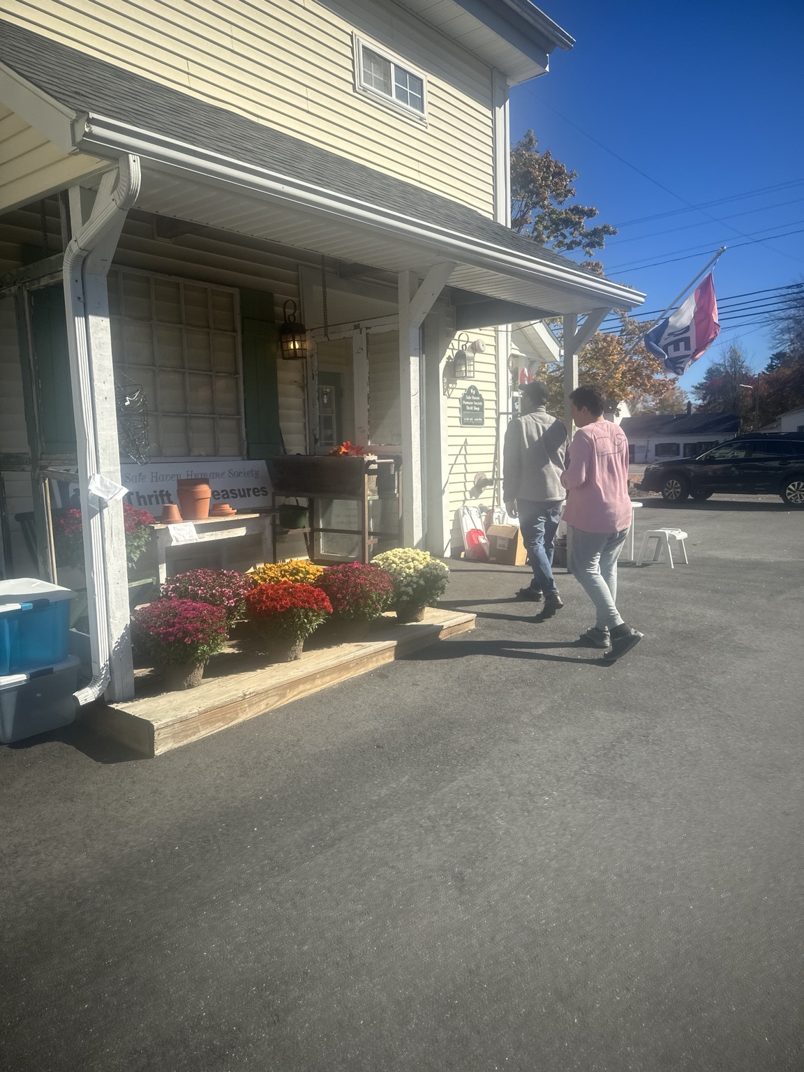 Two family members outside Safe Haven Humane Society’s thrift shop, beside autumn flowers and the covered yellow storefront.