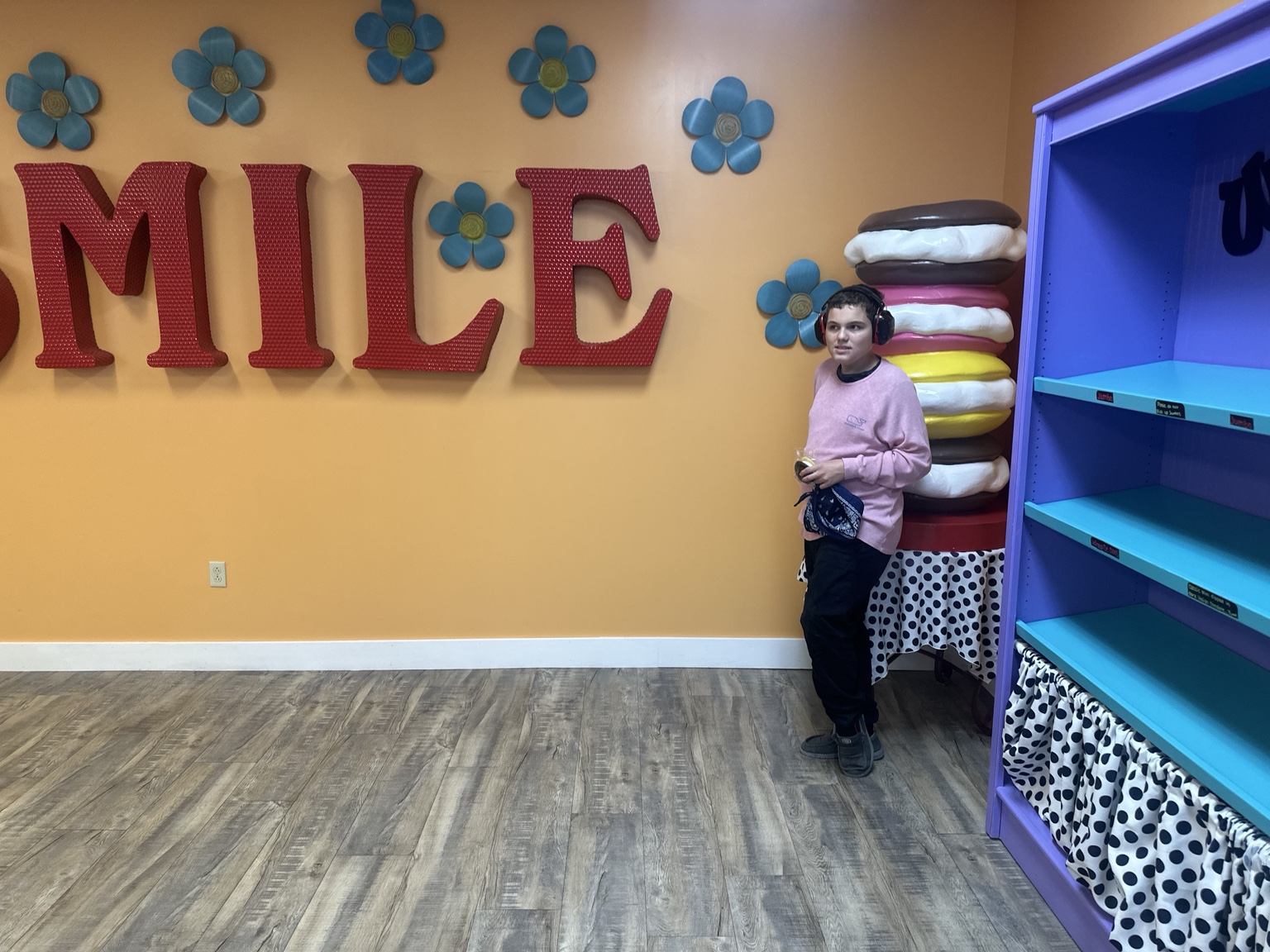 James beside a smaller whoopie-pie display, with large red SMILE lettering, blue flowers, orange walls and purple shelving around him.